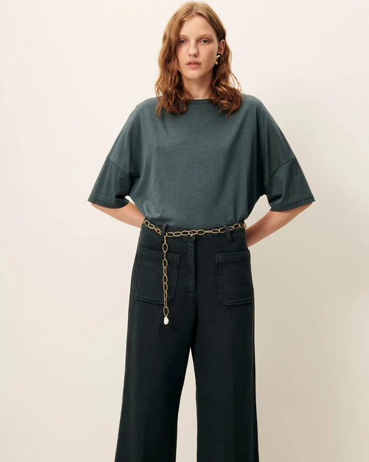 Model is wearing an oversized green T-shirt with green pants and a chain belt. White background