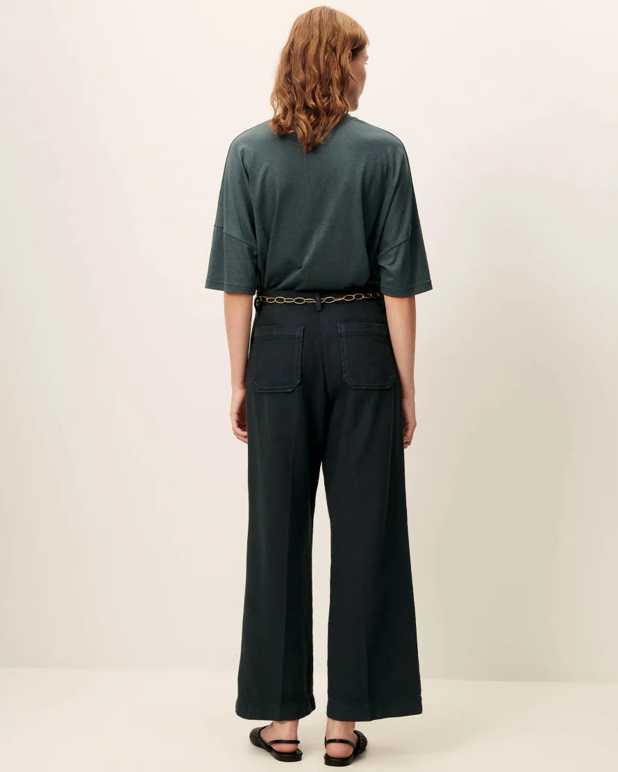 Back view of a model wearing an oversized green T-shirt with green pants and a chain belt. White background