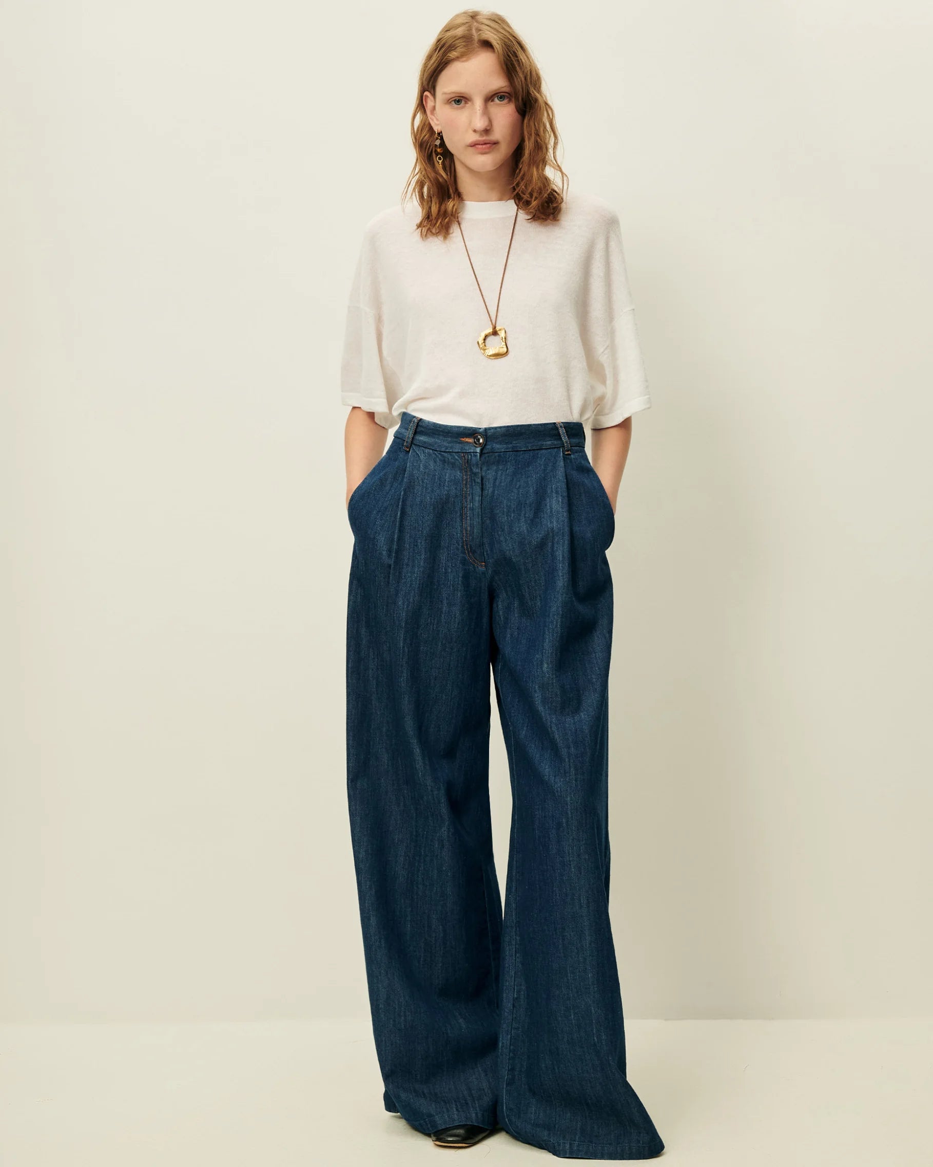 Woman wearing a white top and blue wide-leg pants on a plain background