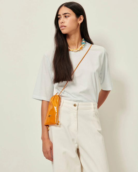 Model wearing an ice blue T-shirt with white jeans, a yellow necklace and cross body bag. White background