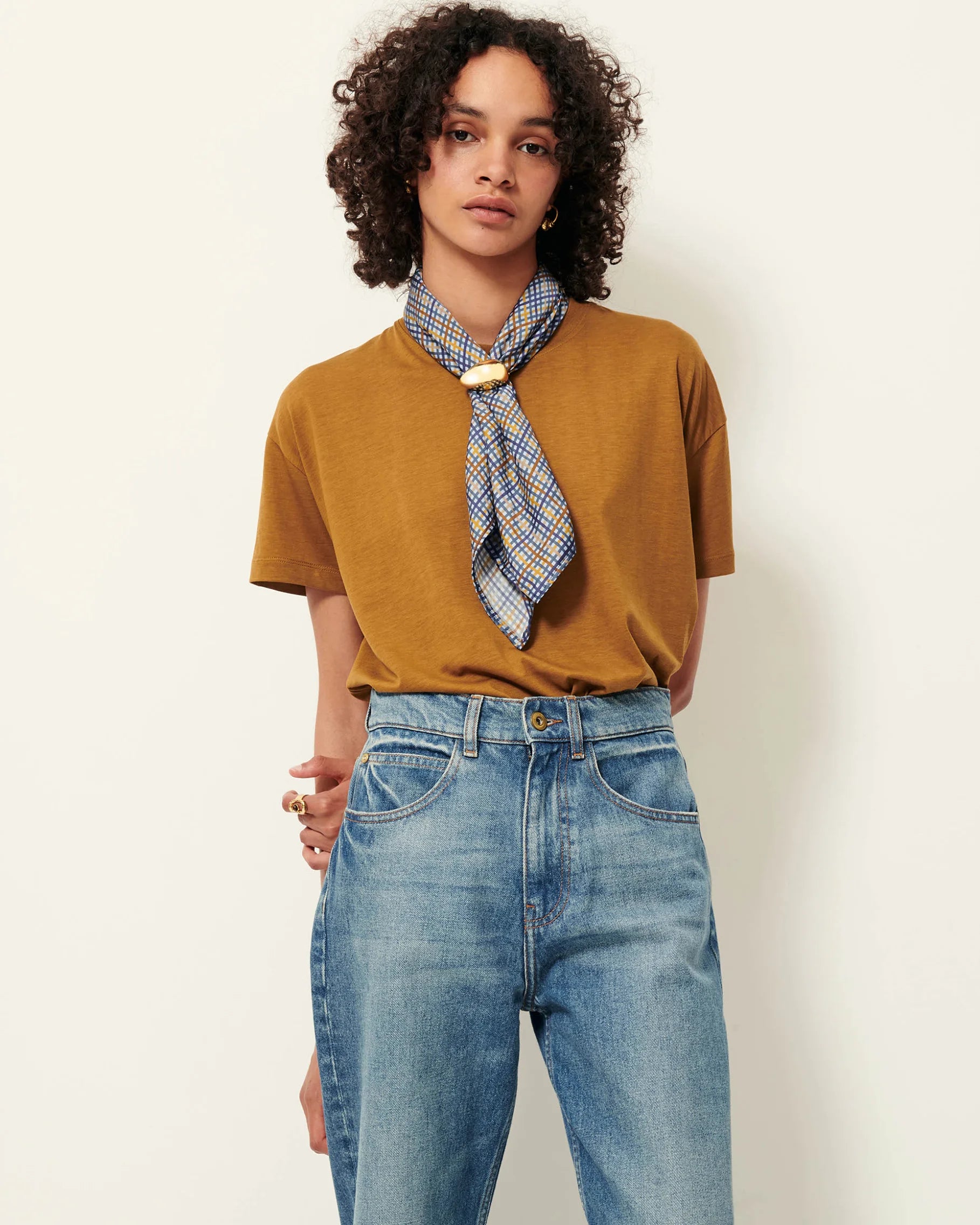 Model wearing a bronze short sleeve T-Shirt with a scarf and jeans. White background