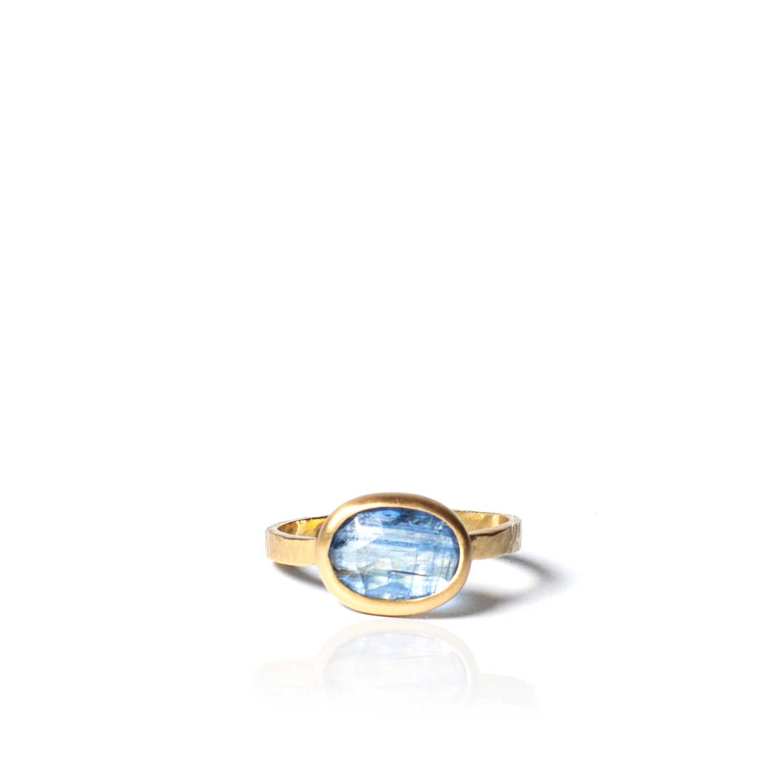 A gold ring with an oval-shaped, light blue cabochon gemstone, shown on a clean white background with a soft reflection below.