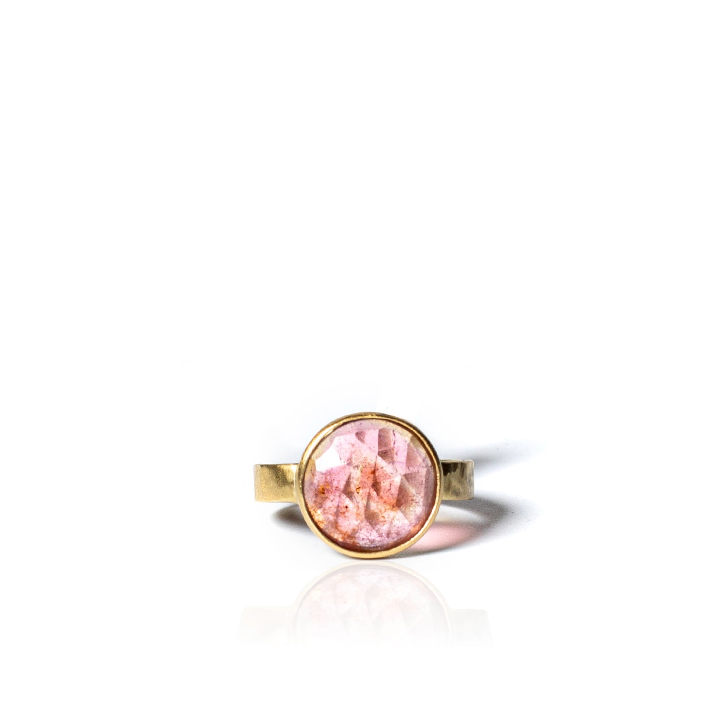 A gold ring with a round bezel-set pink stone, shown on a clean white background with a soft reflection below.