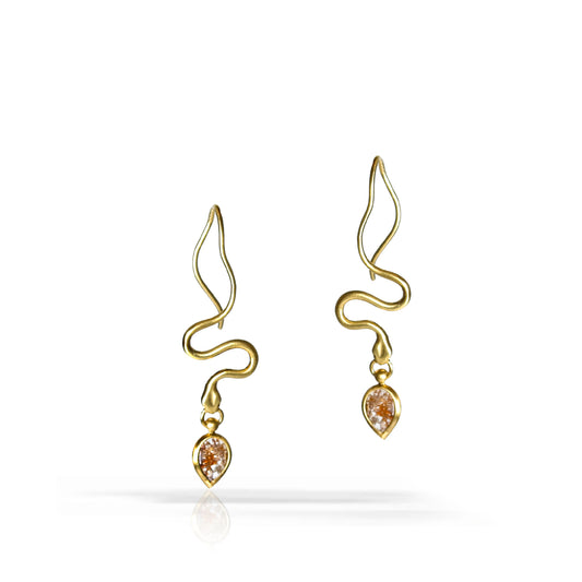 A pair of gold dangle earrings with a wavy, snake-like wire design and a small teardrop-shaped clear gemstone at the bottom, shown on a white background with a soft reflection.