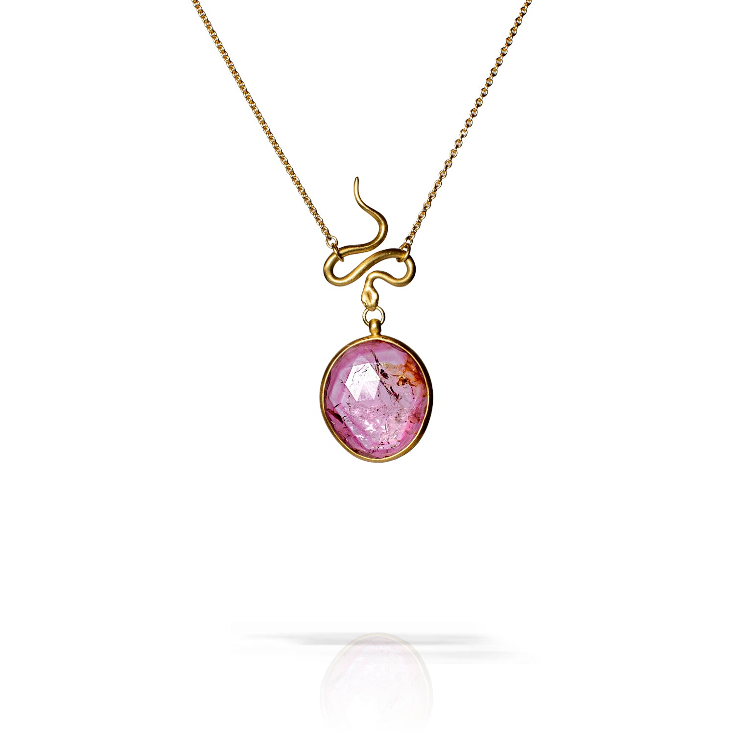 A gold pendant necklace featuring a circular faceted purple gemstone with inclusions, suspended from a curved gold chain, shown against a white background with a soft reflection below.