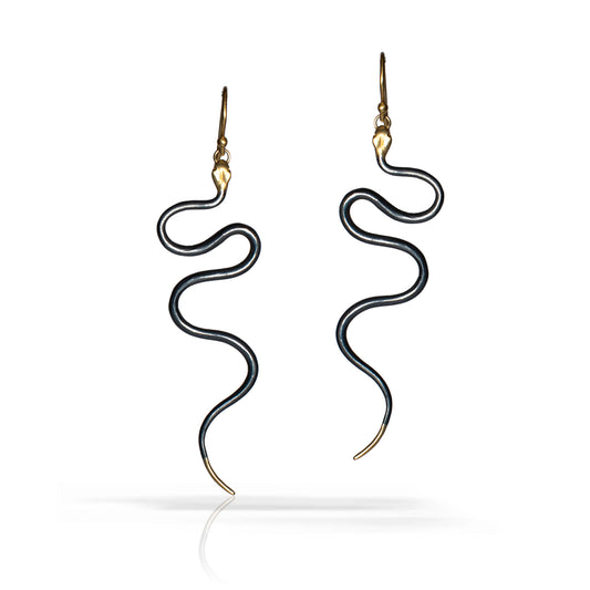 A pair of snake-shaped drop earrings with black bodies and gold-toned heads, hooks, and tips, shown on a clean white background with a soft reflection below.