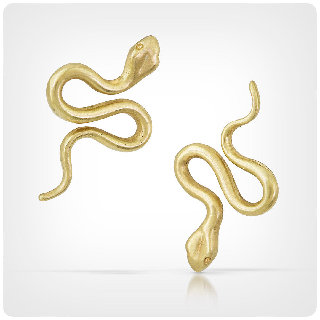 A pair of gold snake-shaped stud earrings on a light gray background with a subtle reflection.