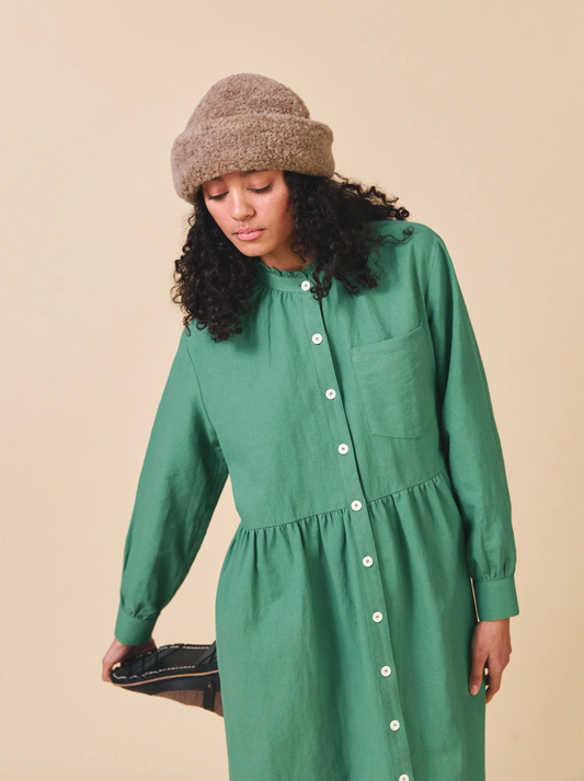 Woman wearing a green dress with white buttons and a brown knit hat on a beige background