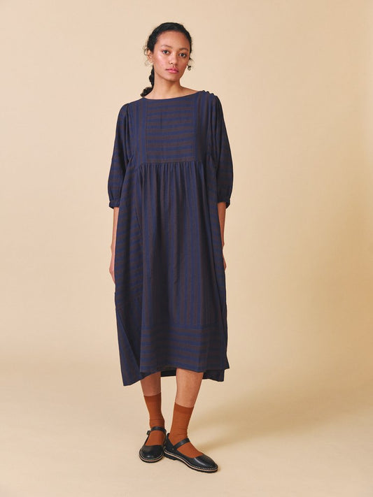 Woman wearing a navy dress with puffed sleeves against a beige background