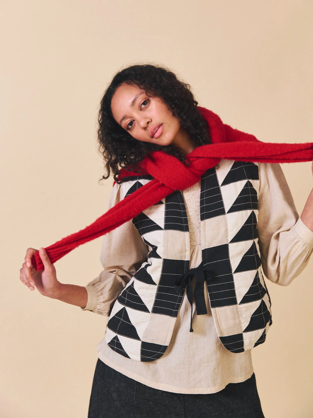 Woman wearing a geometric patterned vest and red scarf against a beige background