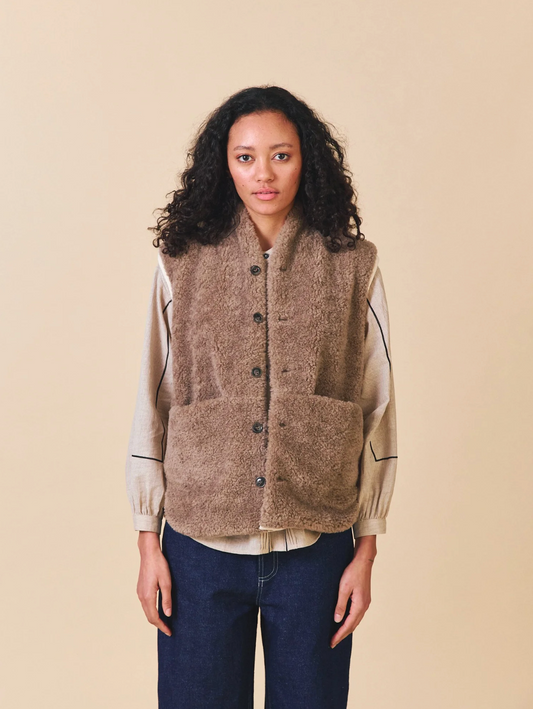 Woman wearing a brown vest over a light shirt with a beige background