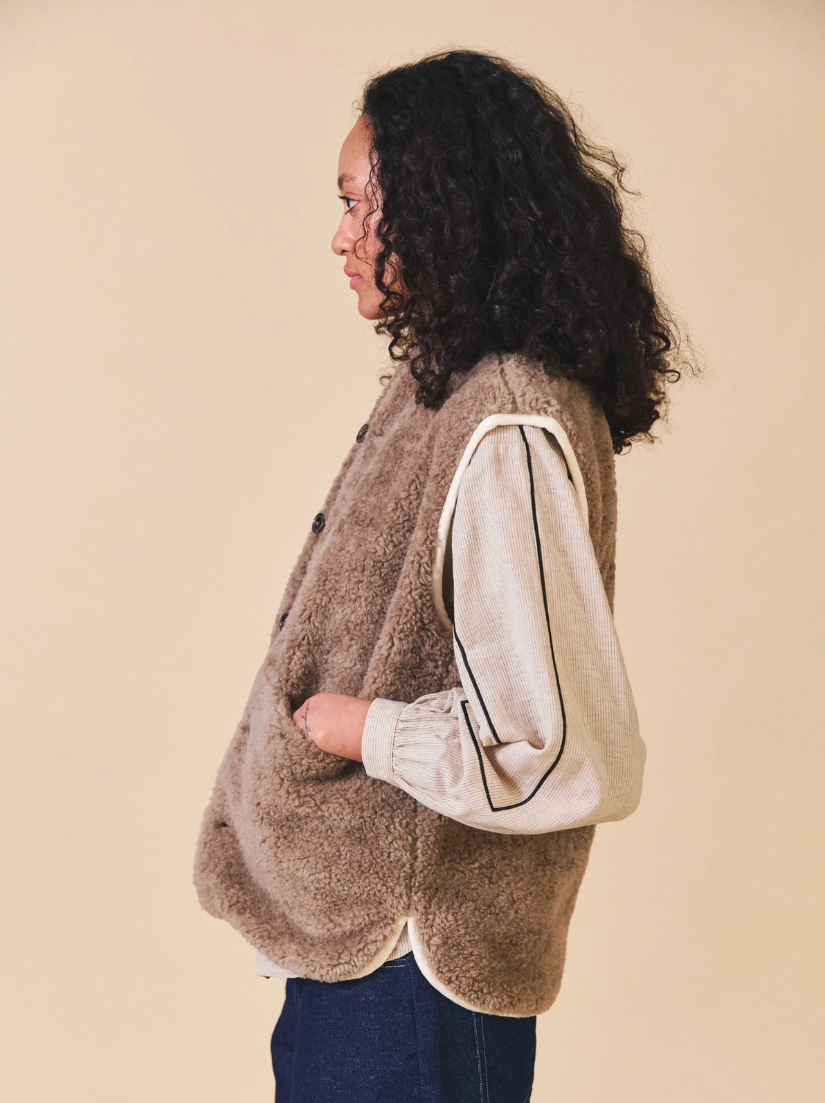 Person wearing a brown vest over a white shirt with black trim on a beige background
