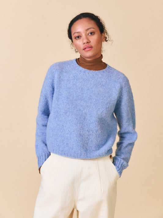 Woman wearing a blue sweater and white pants against a beige background