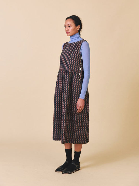 Woman wearing a patterned dress over a blue turtleneck on a beige background