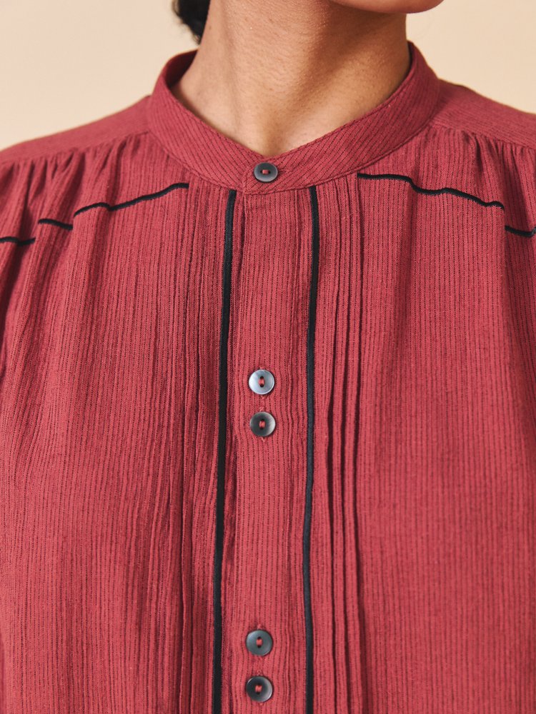 Close-up of a red textured shirt with black piping and buttons on a beige background