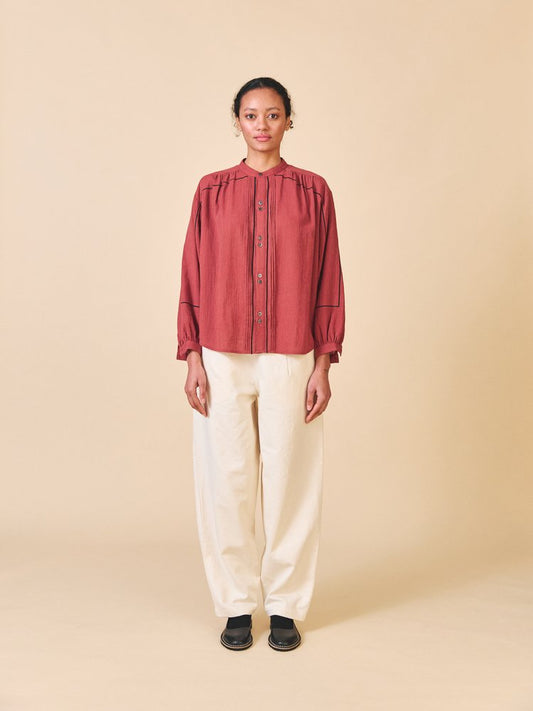 Person wearing a red blouse and beige pants on a beige background