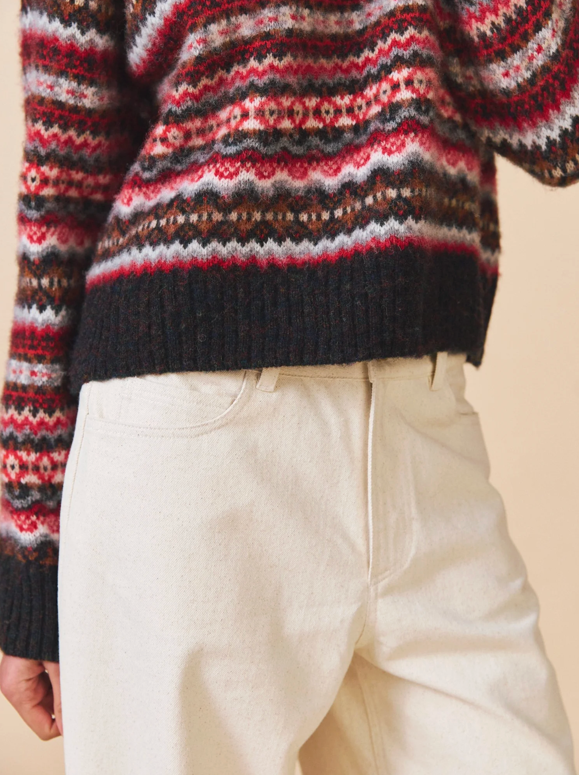Person wearing a patterned sweater and light-colored pants on a beige background