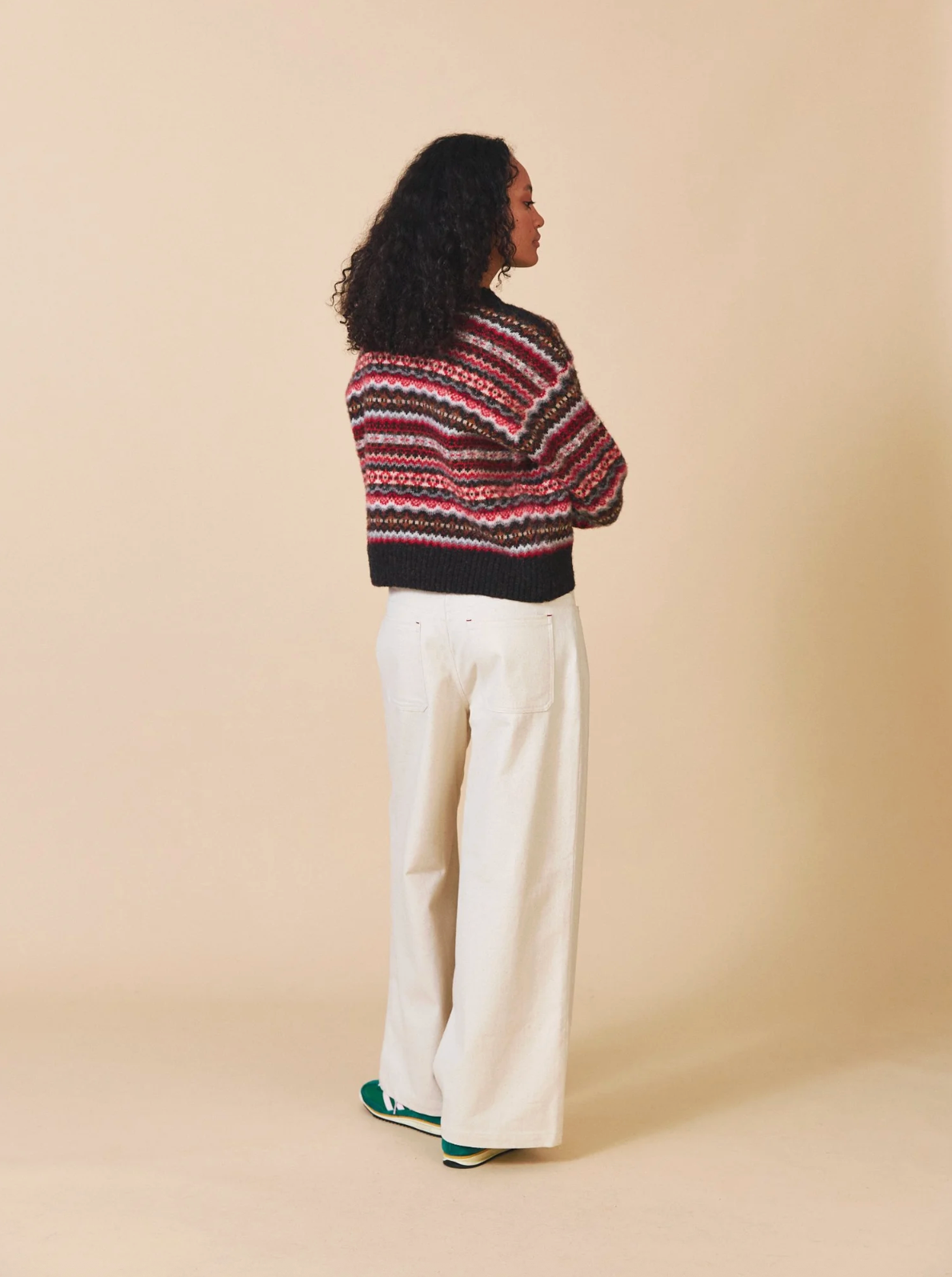 Person wearing a patterned sweater and white pants on a beige background