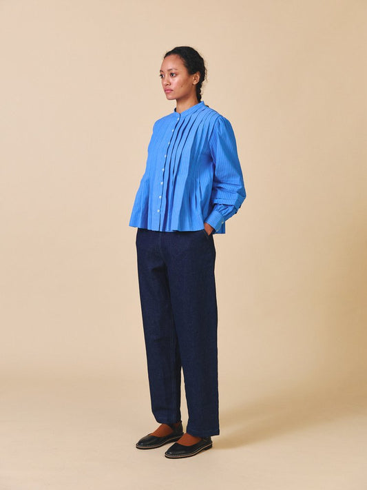 Person wearing a blue pleated blouse and navy pants on a beige background