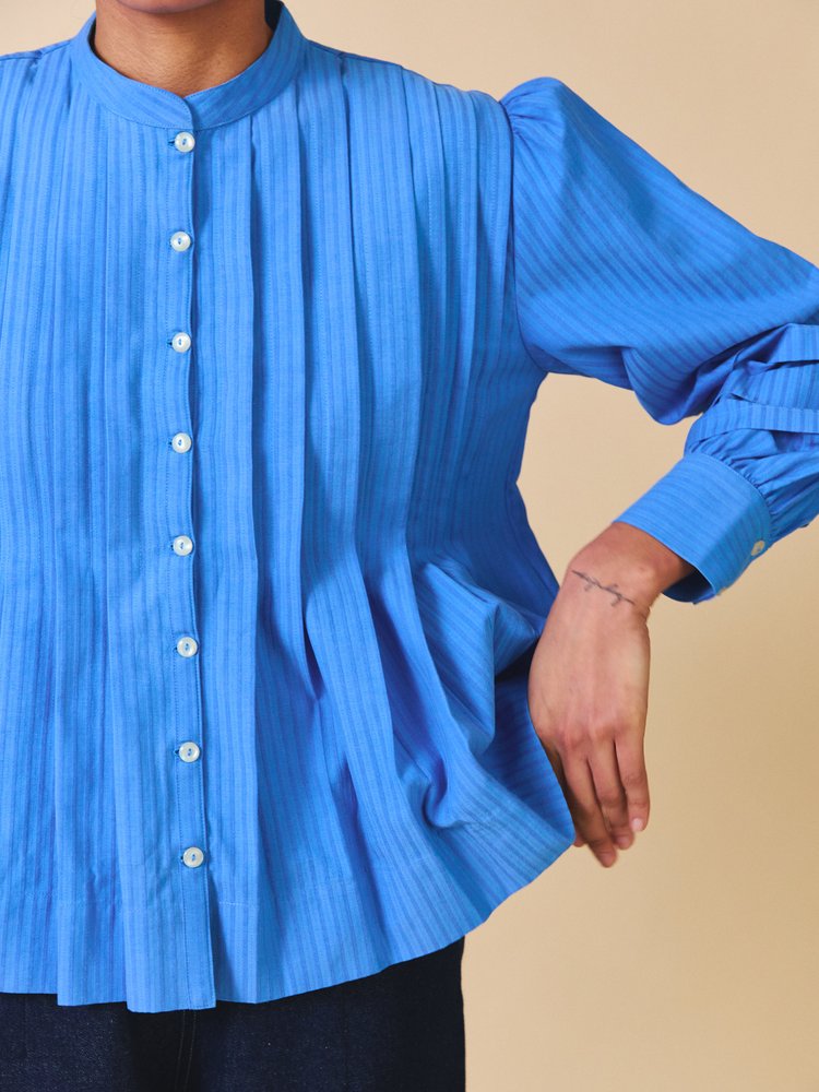 Blue pleated shirt worn by a person on a beige background