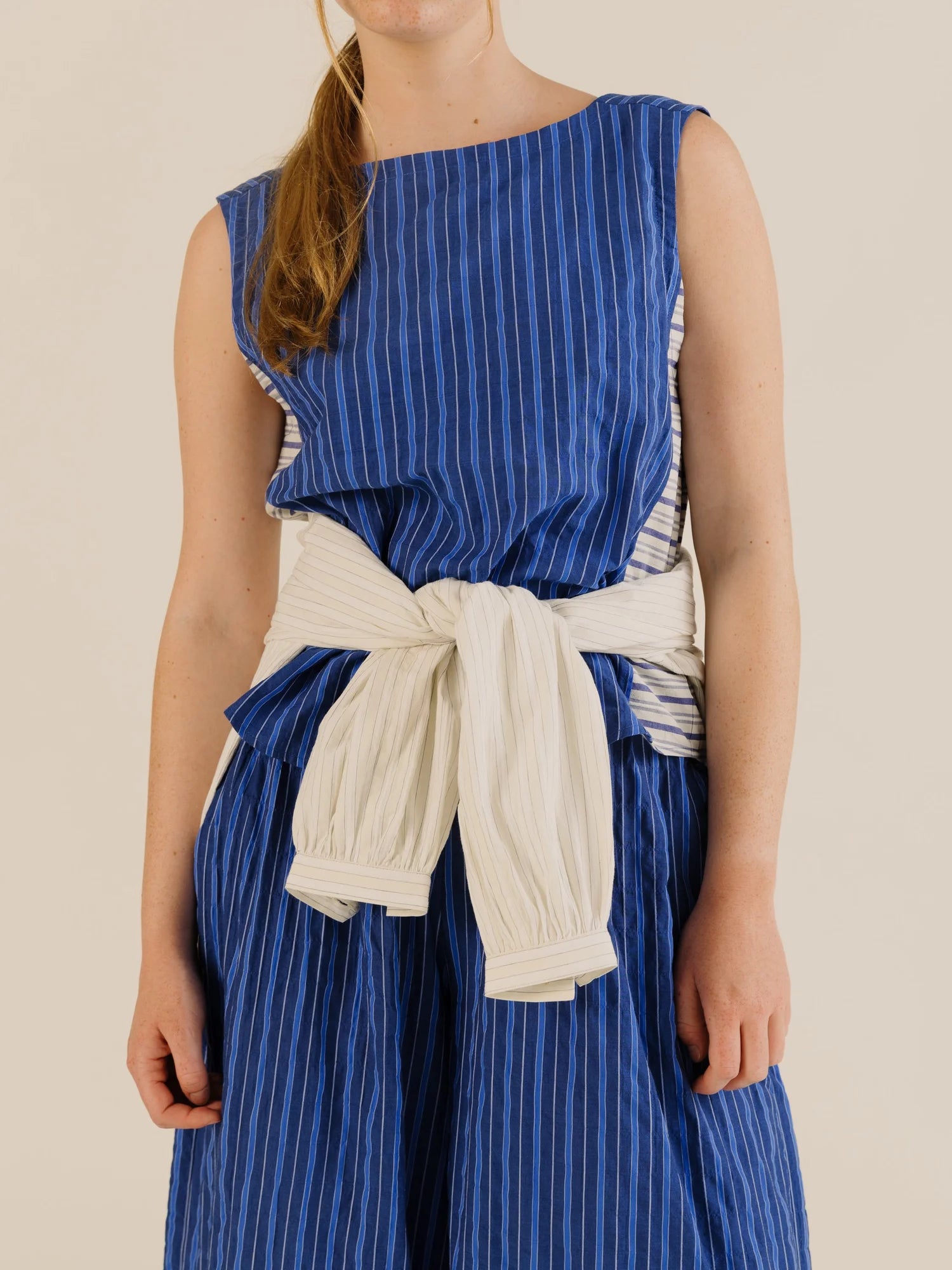 Front view of stripe sleeveless top and pant with a light colour top tied at the model's waist 