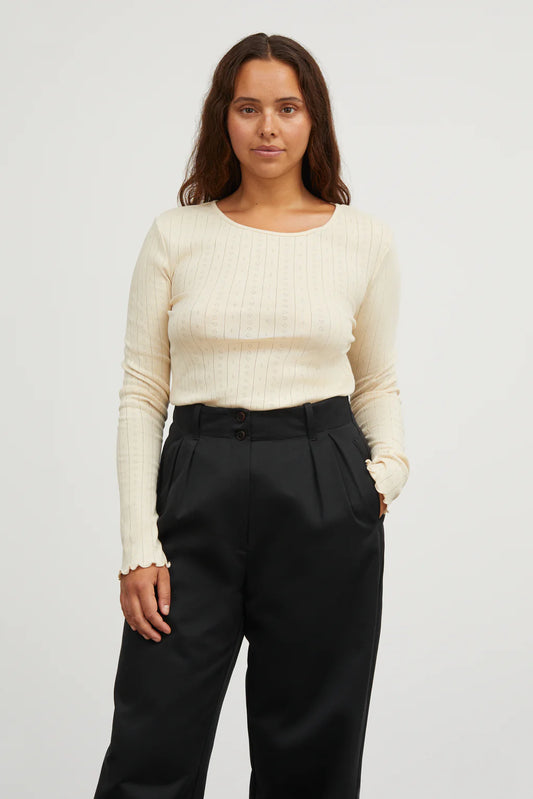 Woman wearing a cream sweater and black pants against a white background