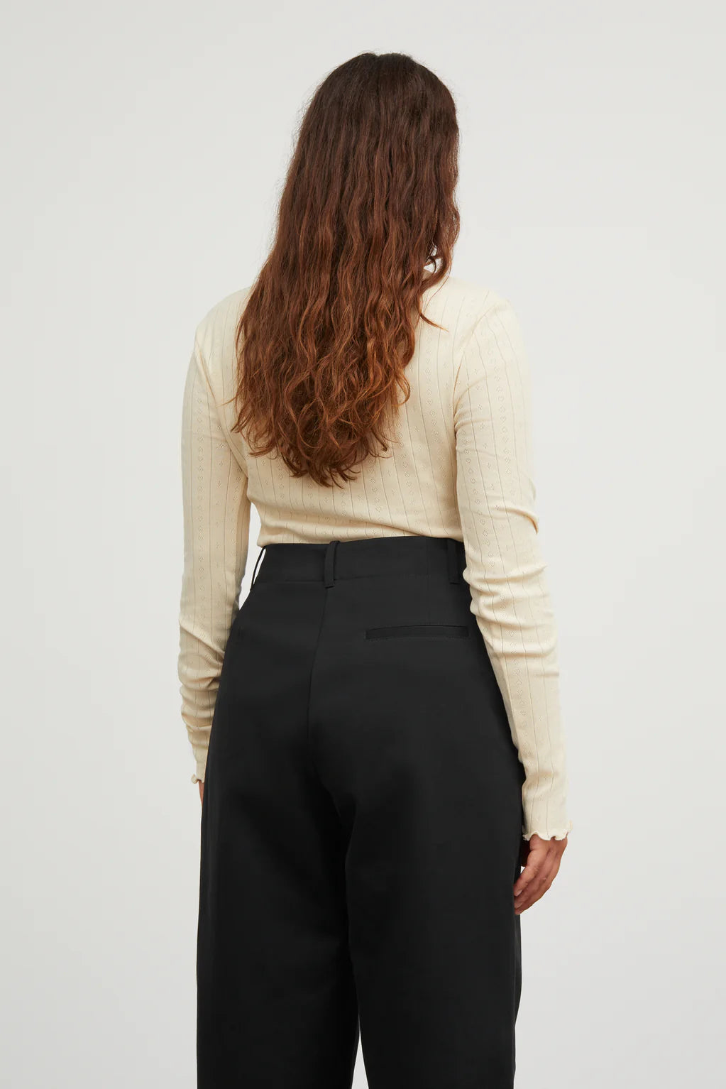 Person wearing a beige long-sleeve top and black pants on a plain background