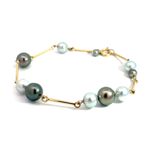 A gold bracelet featuring a series of round freshwater pearls in white, pale blue, and dark green-gray tones, displayed on a clean white background.