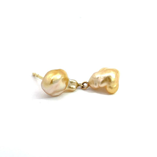 A pair of gold stud earrings featuring irregular, baroque-style freshwater pearls in a champagne-gold color, connected by a small gold chain.
