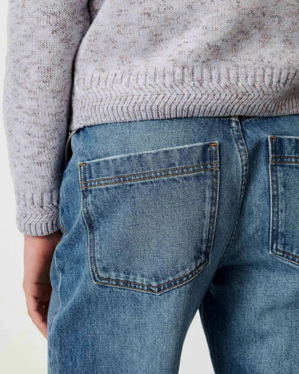 Close-up back view of a person wearing medium-wash blue jeans and a light heather gray knit sweater, showing the back pockets of the jeans.