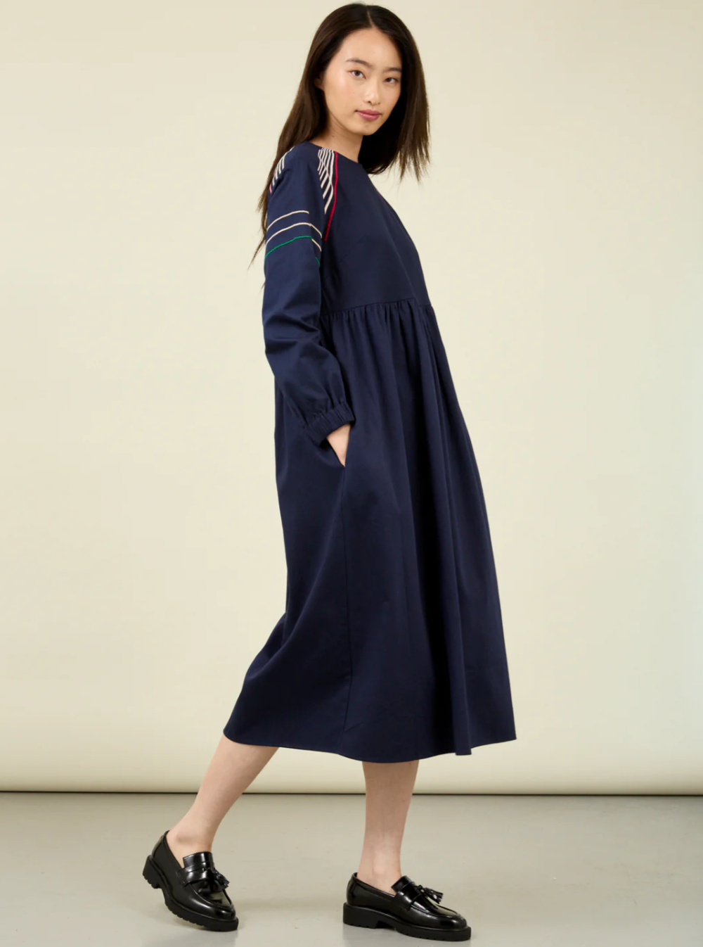 woman with long dark hair wearing blue dress with embroidered linear design.