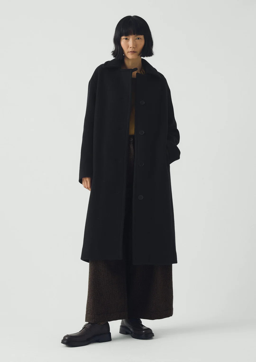 Person wearing a long black coat on a white background