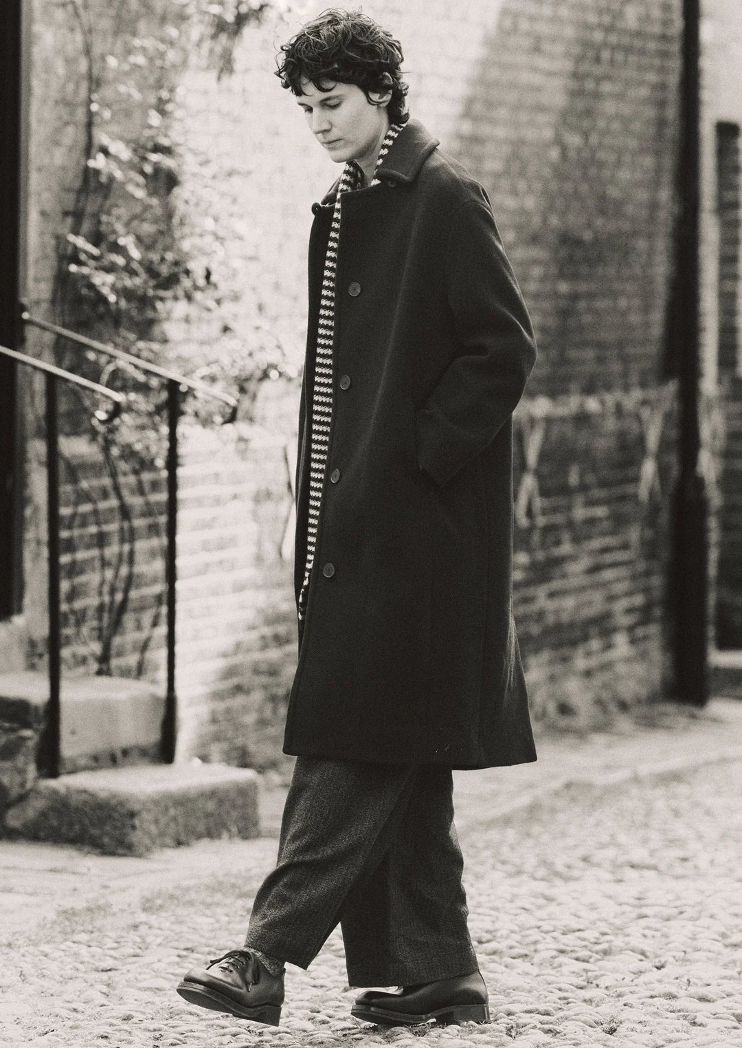 Person wearing a long coat and striped shirt walking outdoors.