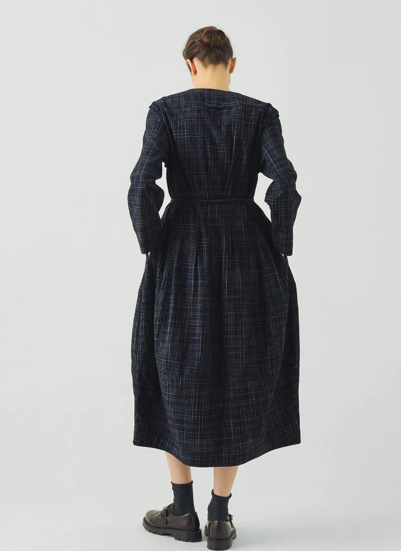 Woman wearing blue checked dress dress against a grey background, rear view