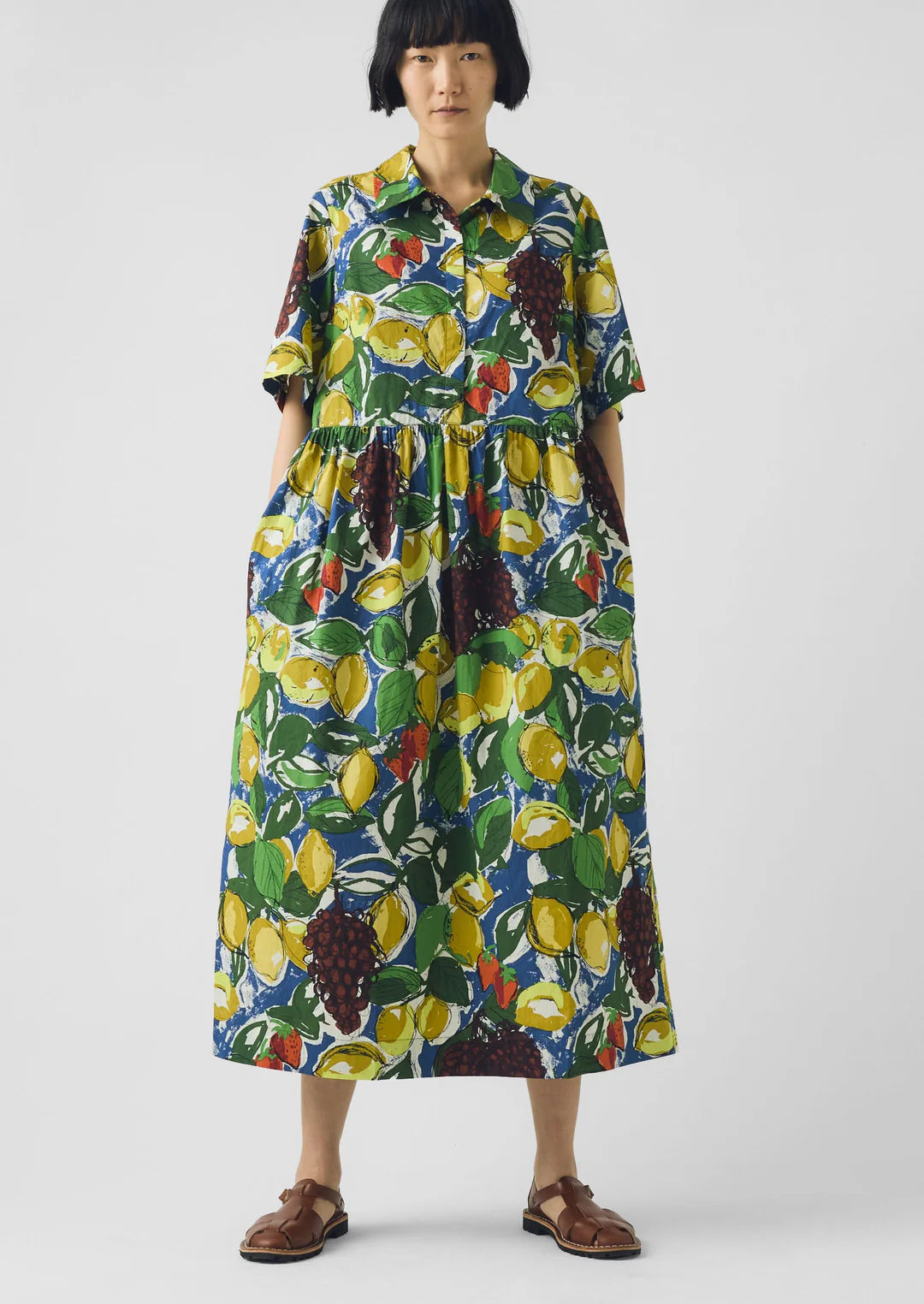 Woman wearing a colorful dress with fruit pattern on a white background