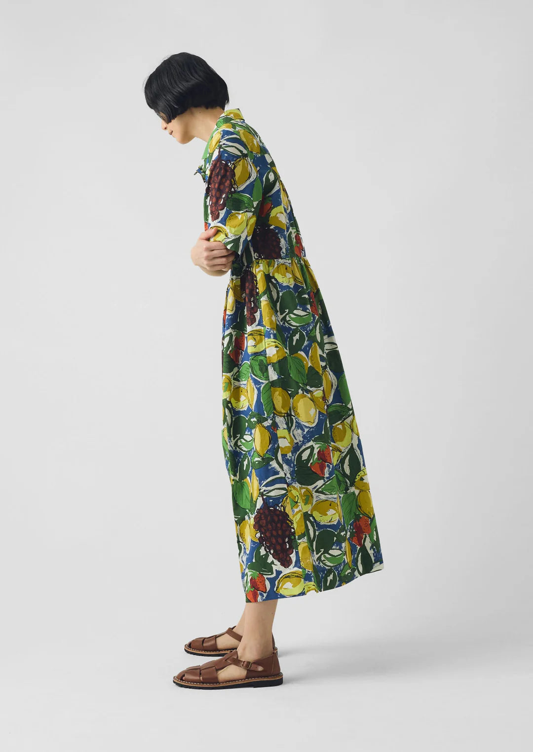 Person wearing a colorful fruit print dress on a plain background
