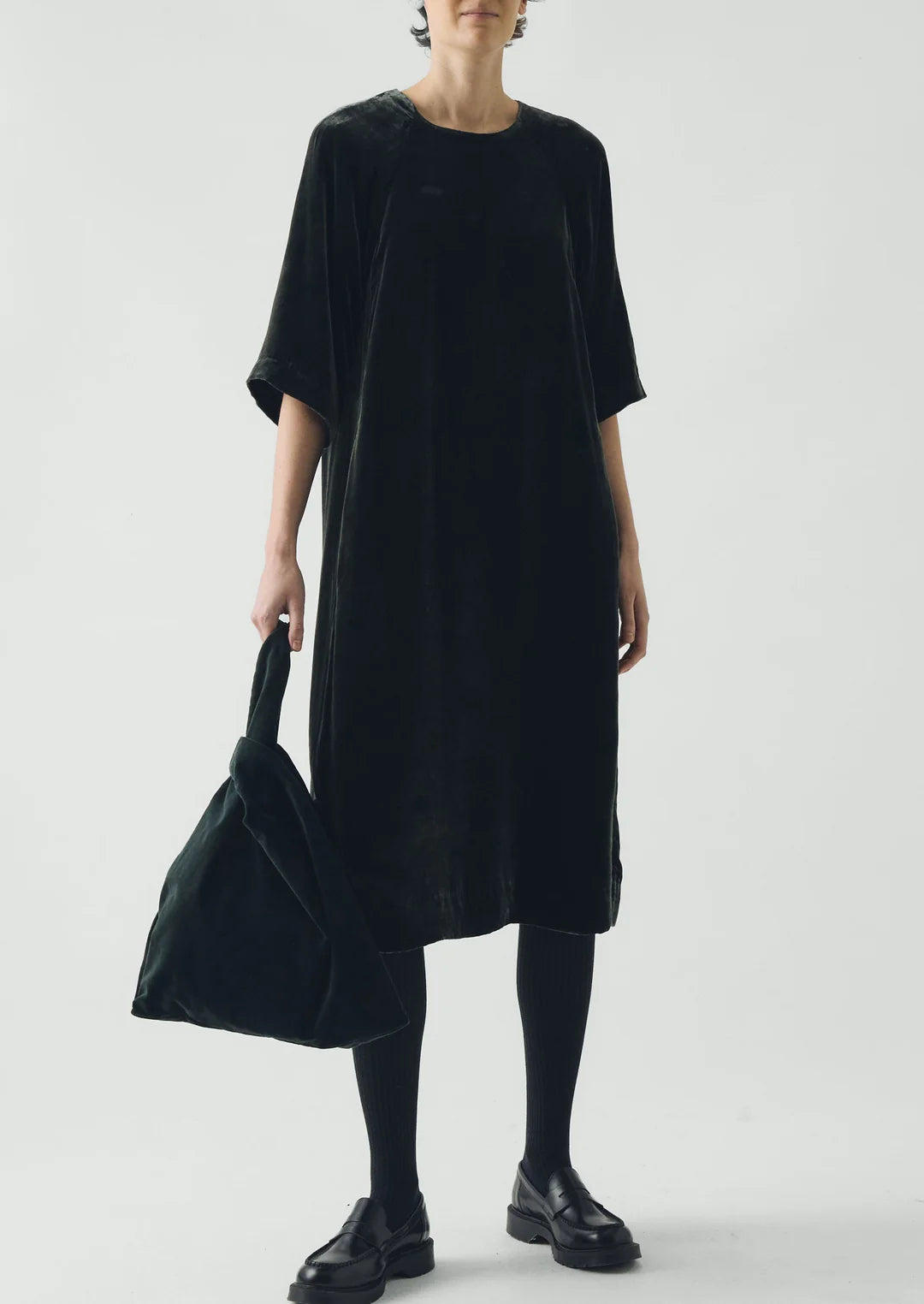 Person wearing a black dress holding a matching bag against a white background