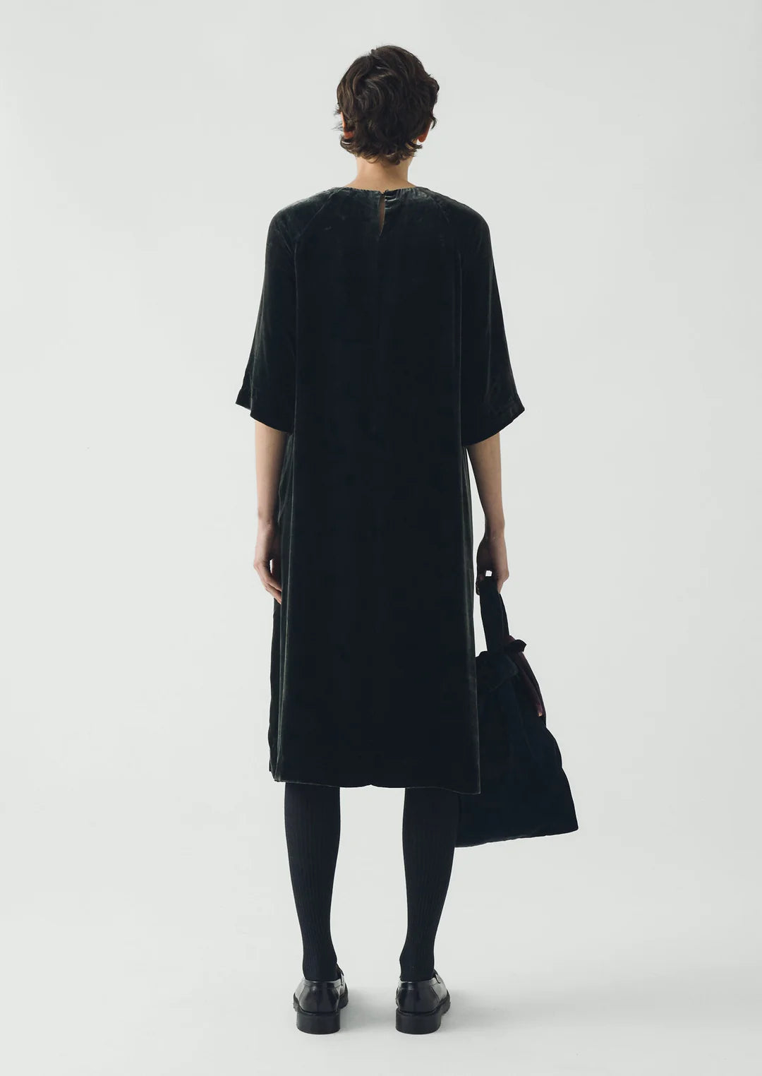 Person wearing a black dress holding a black bag on a white background