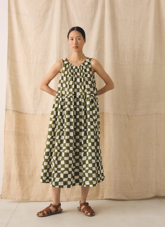Woman wearing a green and white checkered dress against a beige curtain background