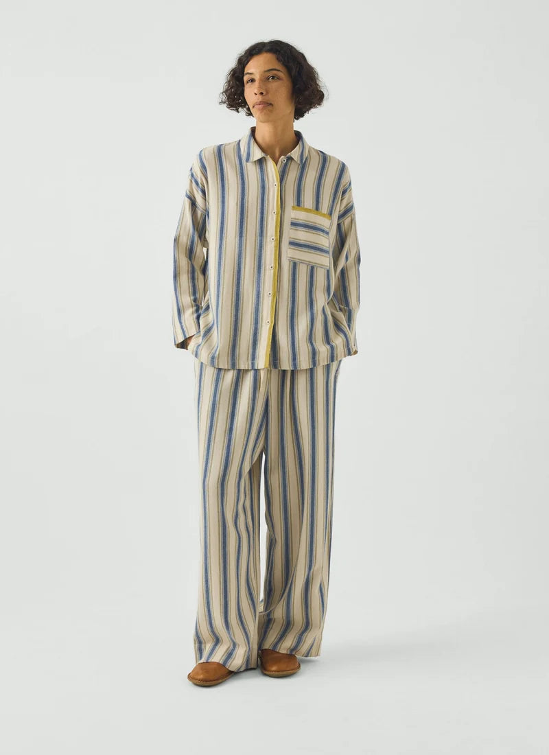 A model wearing a pajama set with blue and cream vertical stripes and a gooseberry-colored trim.