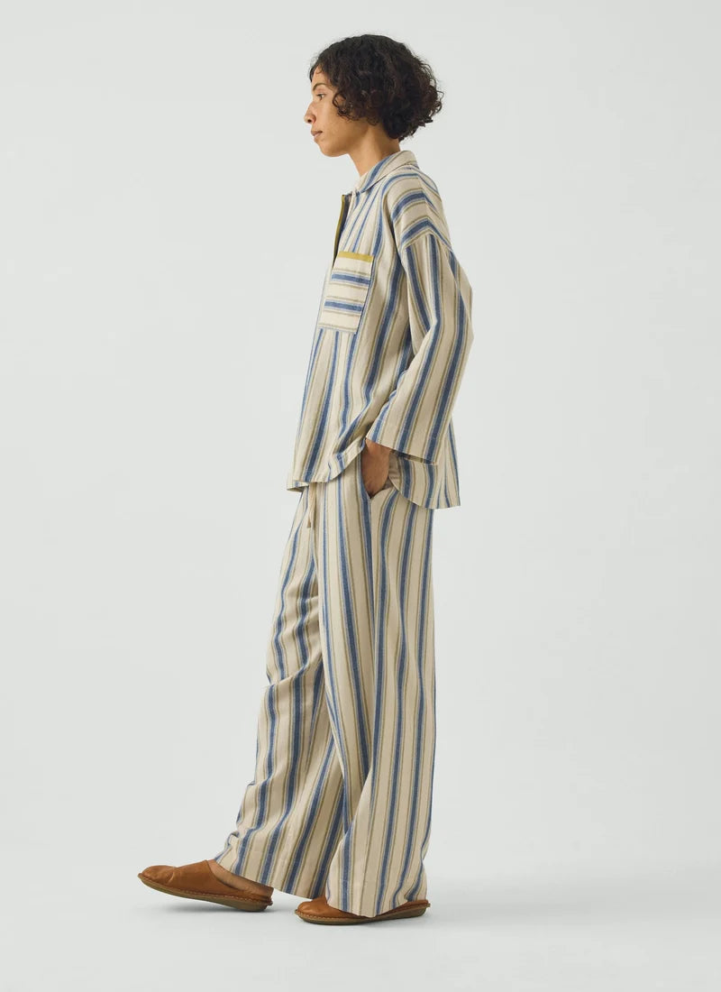 A model wearing a pajama set with blue and cream vertical stripes and a gooseberry-colored trim.