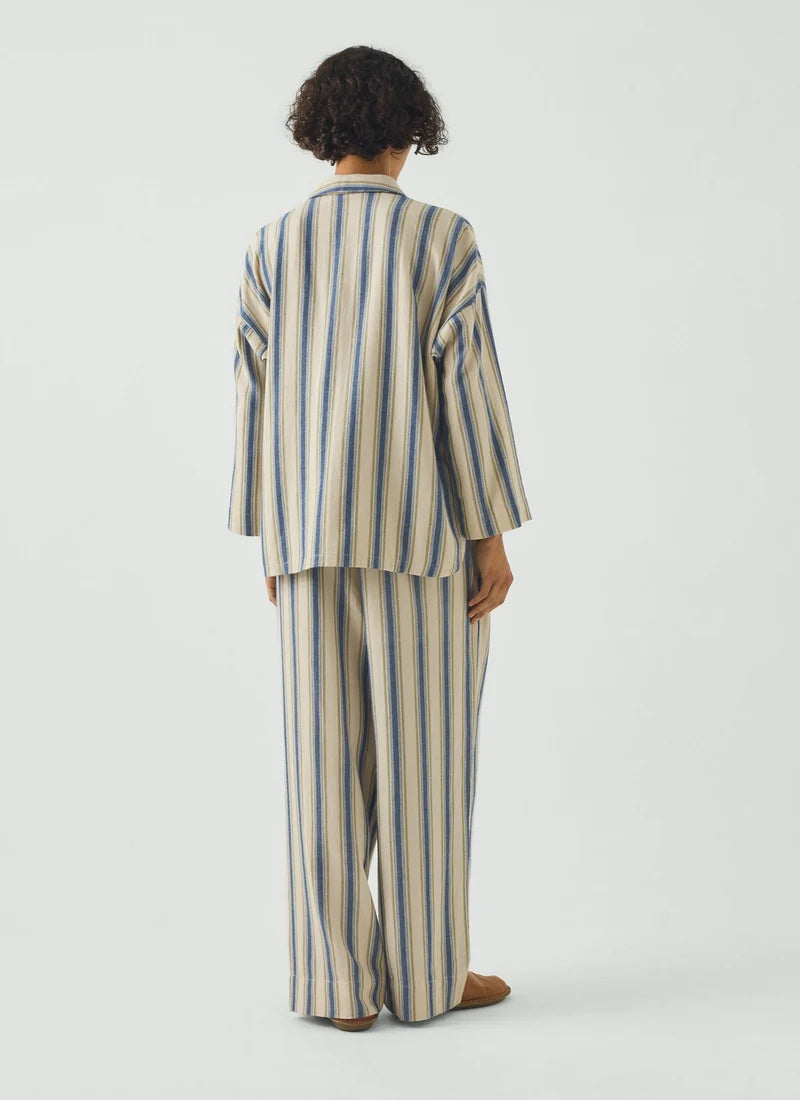 A model wearing a pajama set with blue and cream vertical stripes and a gooseberry-colored trim.
