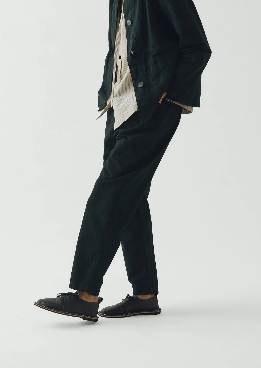 Person wearing a dark green coat and pants with black shoes on a white background