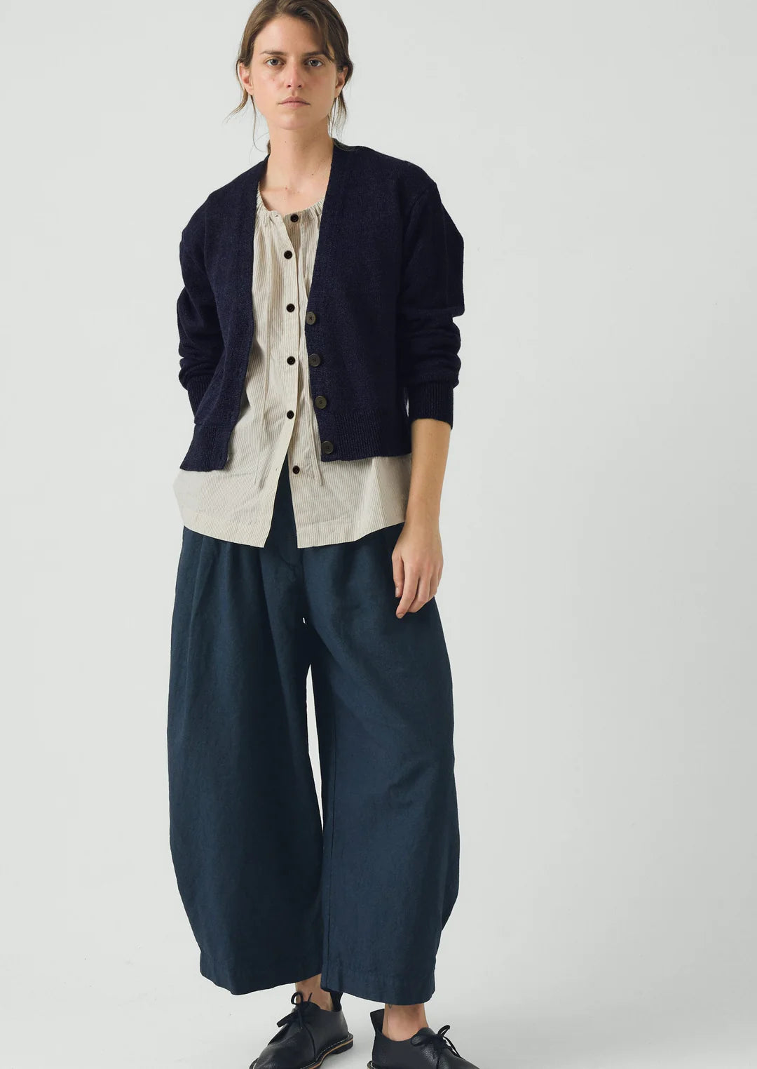Person wearing a navy cardigan, beige shirt, and dark blue wide-leg pants on a white background