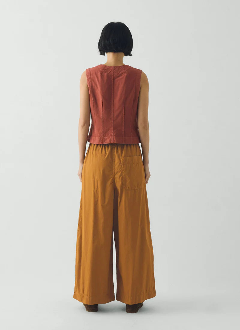 Person wearing a rust-colored sleeveless top and wide-leg pants on a white background
