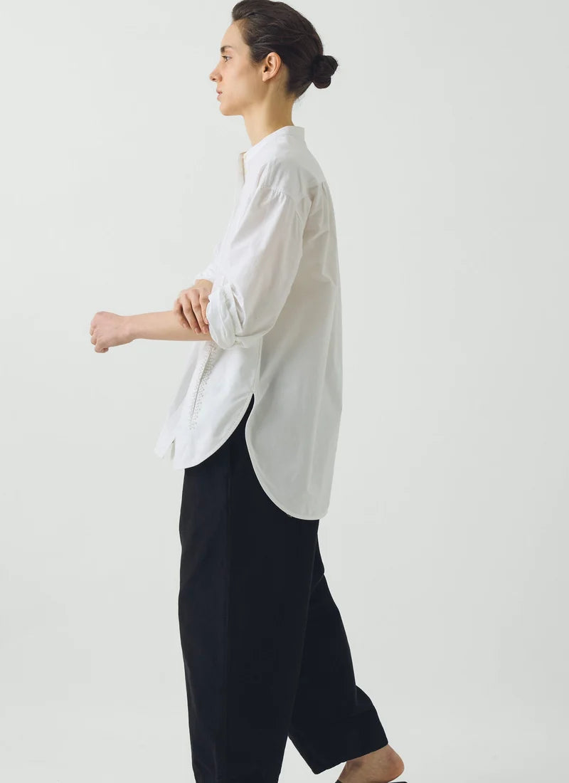 A model wearing a long-sleeve white shirt and navy pants standing against a white background.