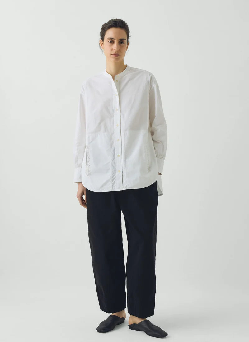 A model wearing a long-sleeve white shirt and navy pants standing against a white background.