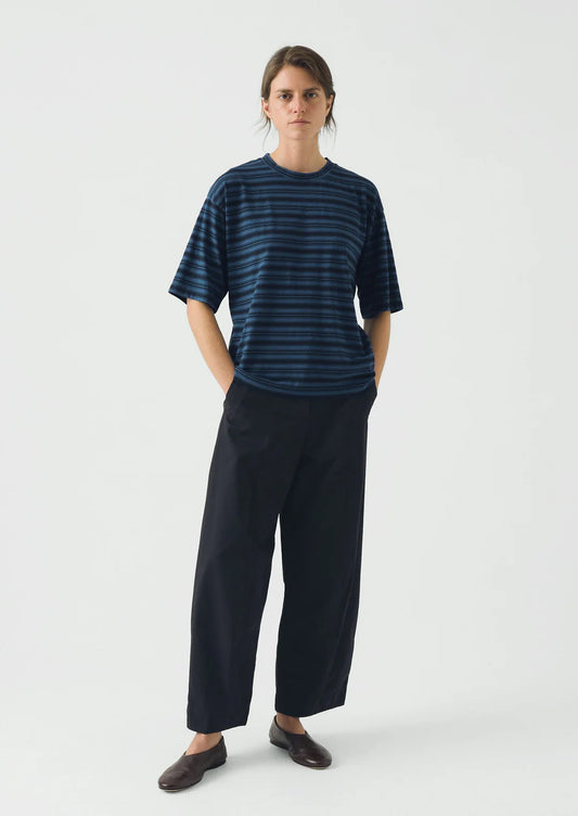 Person wearing a blue striped shirt and black pants on a white background