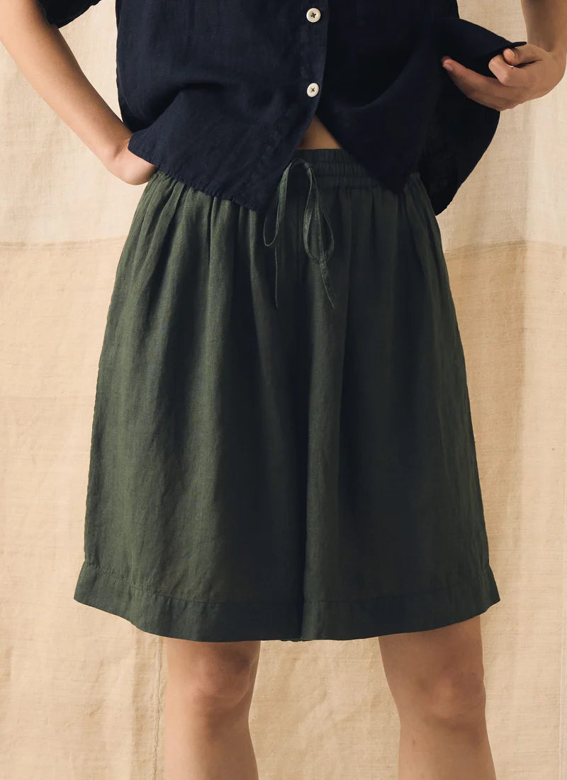 Person wearing dark green shorts and a navy shirt against a beige background