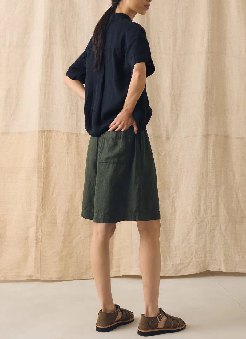Person wearing a navy shirt and green shorts against a beige curtain background